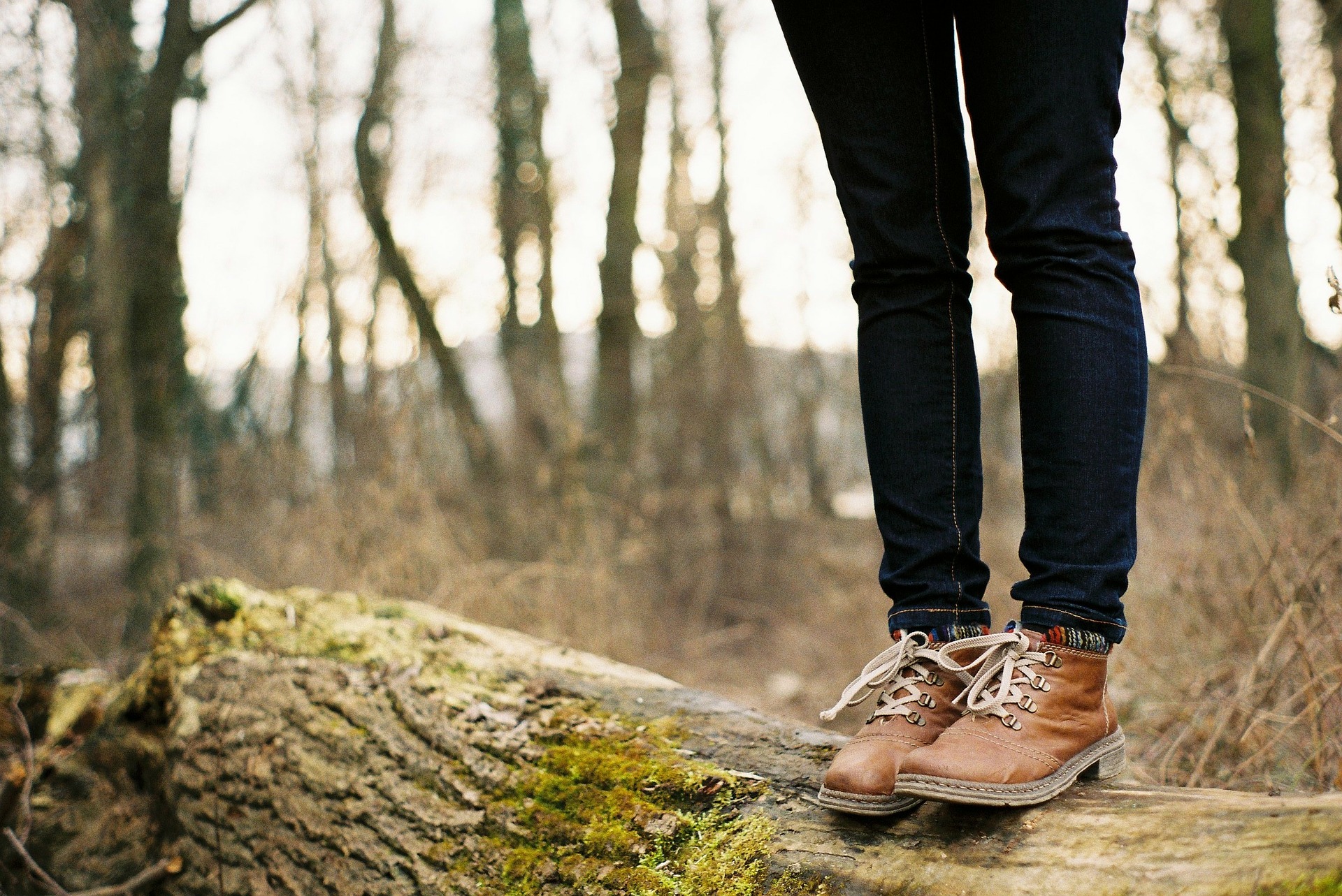 girl with boots standing on a log in the middle of the woods alone