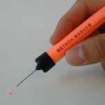  Image of Metron Marker filled with Metron Pink Ink being held over a very small dot that was created with the marker demonstrating delivery precision.